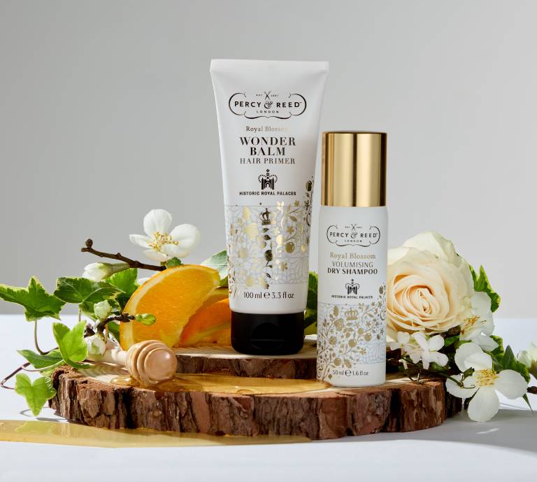 Image of Percy & Reed's Royal Blossom Wonder Balm hair primer and Dry Shampoo on a wooden plinth, surrounded by ivy, orange blossom, honey and jasmine.