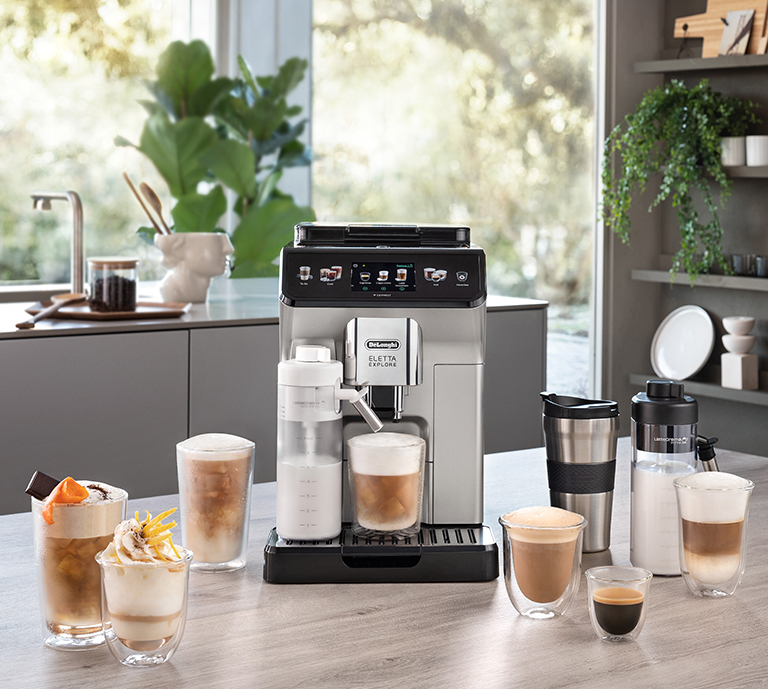Eletta Explore fully automatic coffee machine by De'Longhi. Product is set on a kitchen island surrounded by a variety of drinks that are mad by the machine.