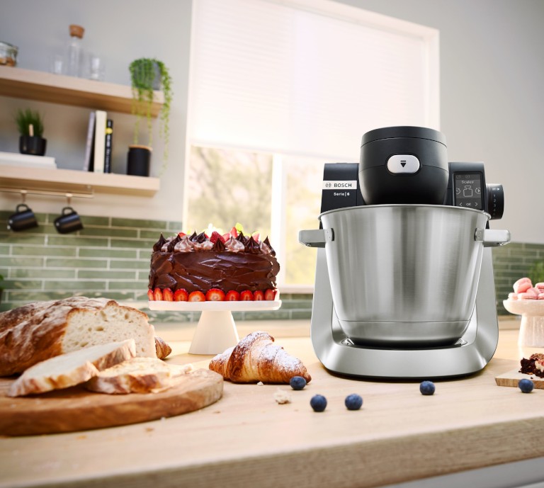 The new Bosch Series 6 stand mixer is shown on a kitchen table with a variety of baked items.