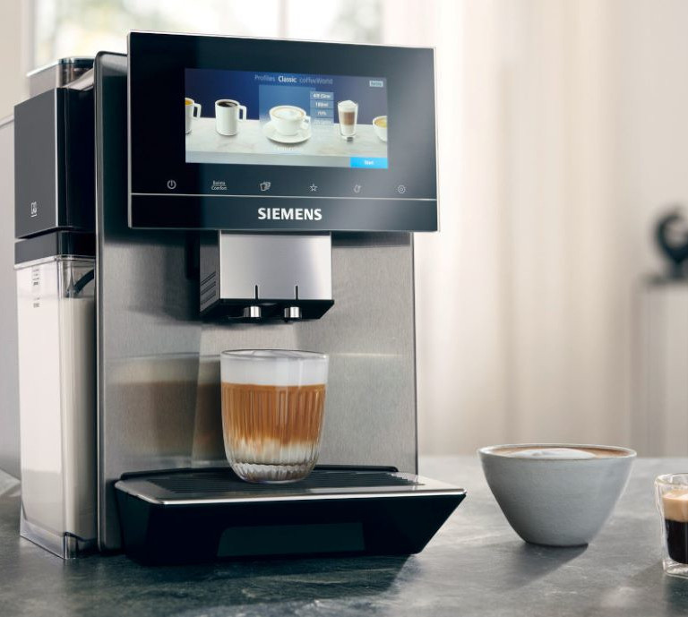 A Siemens bean to cup coffee machine on a couter top with a woman in the background out of focus