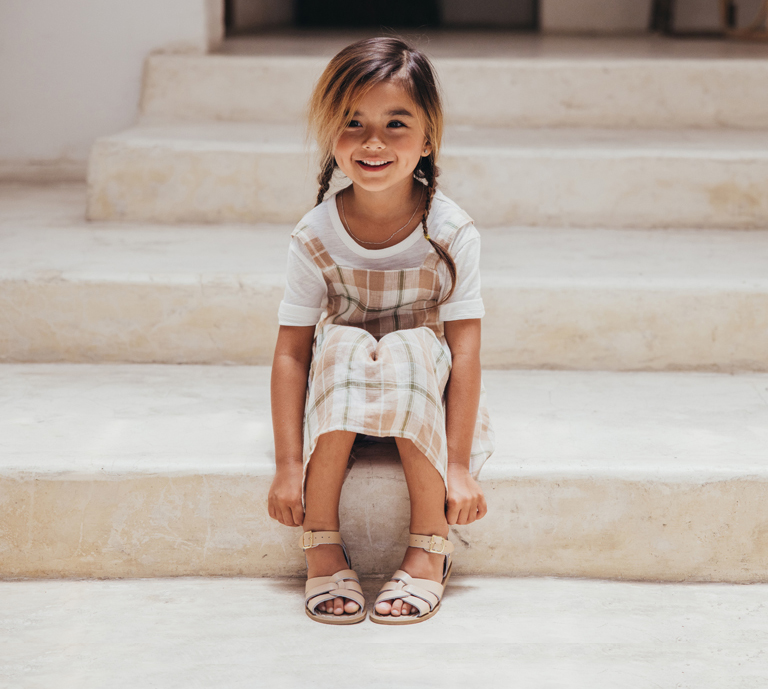 Little girl sits on steps modelling 100% waterprooff leather sqandals ideal for summer