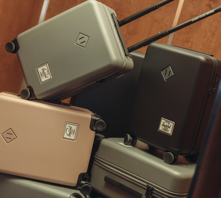 Herschel Supply Co. image of suitcases with a CTA to shop travel essentials